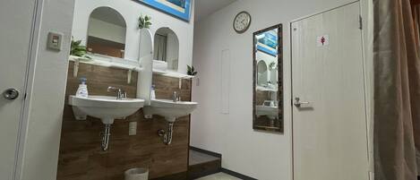 A bathroom with two sinks, a mirror, a clock, and a door with a female restroom symbol.