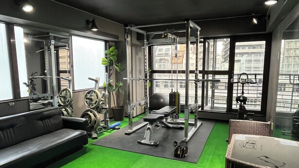 A gym with exercise equipment, a green carpet, a black sofa, and large windows. - Tengcle Stay - Hostel (Tokyo)
