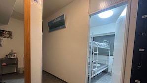 A hotel corridor with bunk beds, a mirror, a shelf with items, and a door with a number. - Tengcle Stay - Hostel (Tokyo)