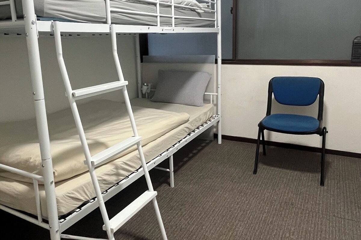 A bunk bed room with a ladder, a chair, and a window.