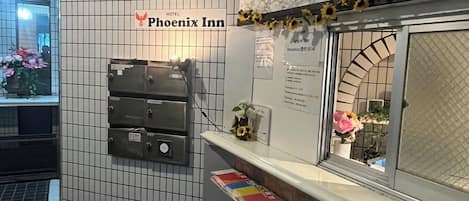 Un área de recepción con un cartel de Phoenix Inn, pared de azulejos, sección de mármol y un mostrador con folletos informativos.