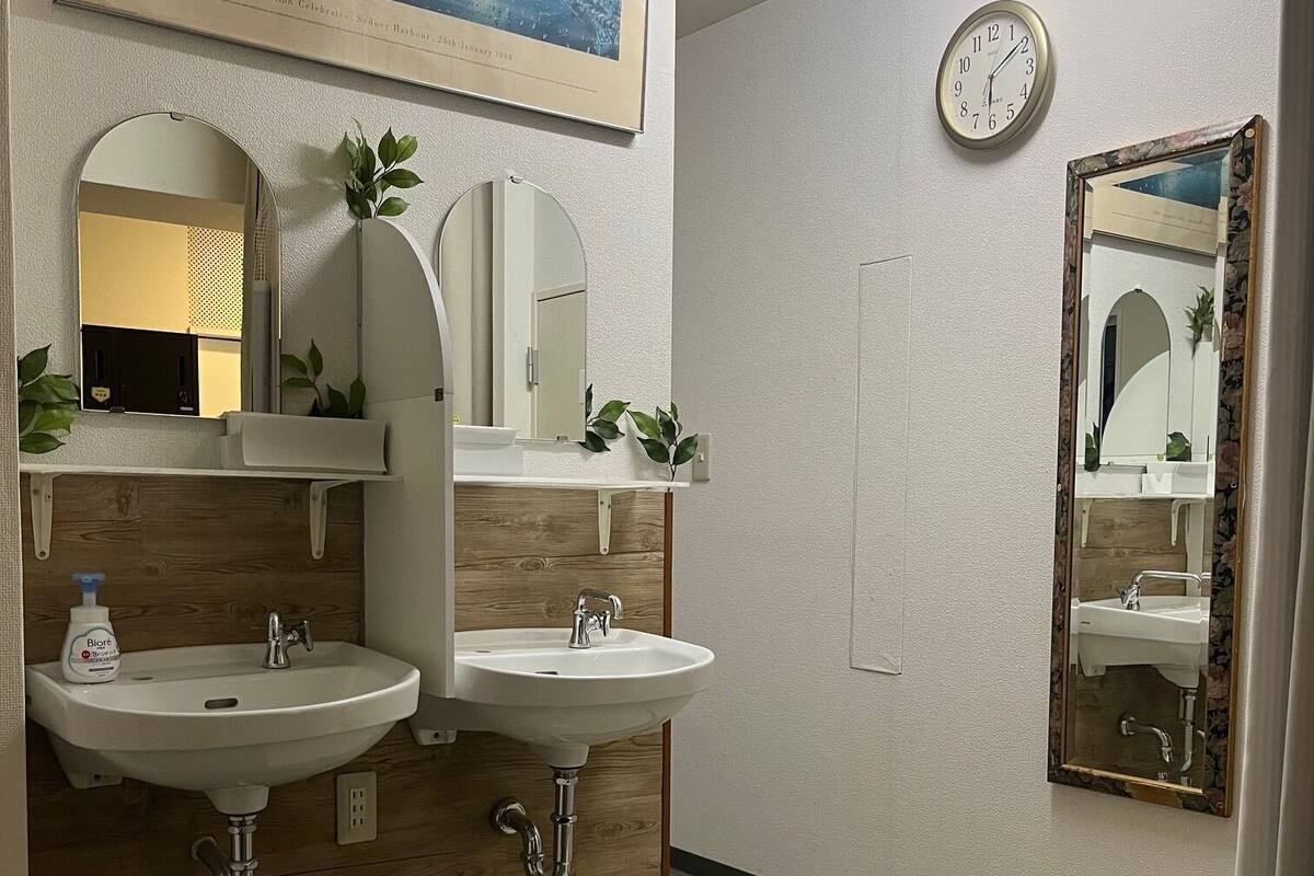 A bathroom with two sinks, a clock, and a framed picture on the wall.