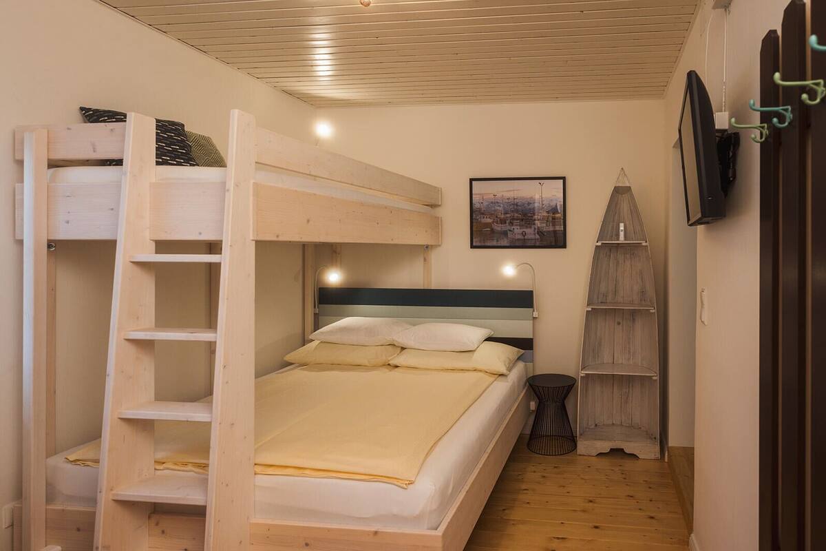 A bunk bed with a ladder, a bedside table, a wall-mounted TV, and a framed picture.