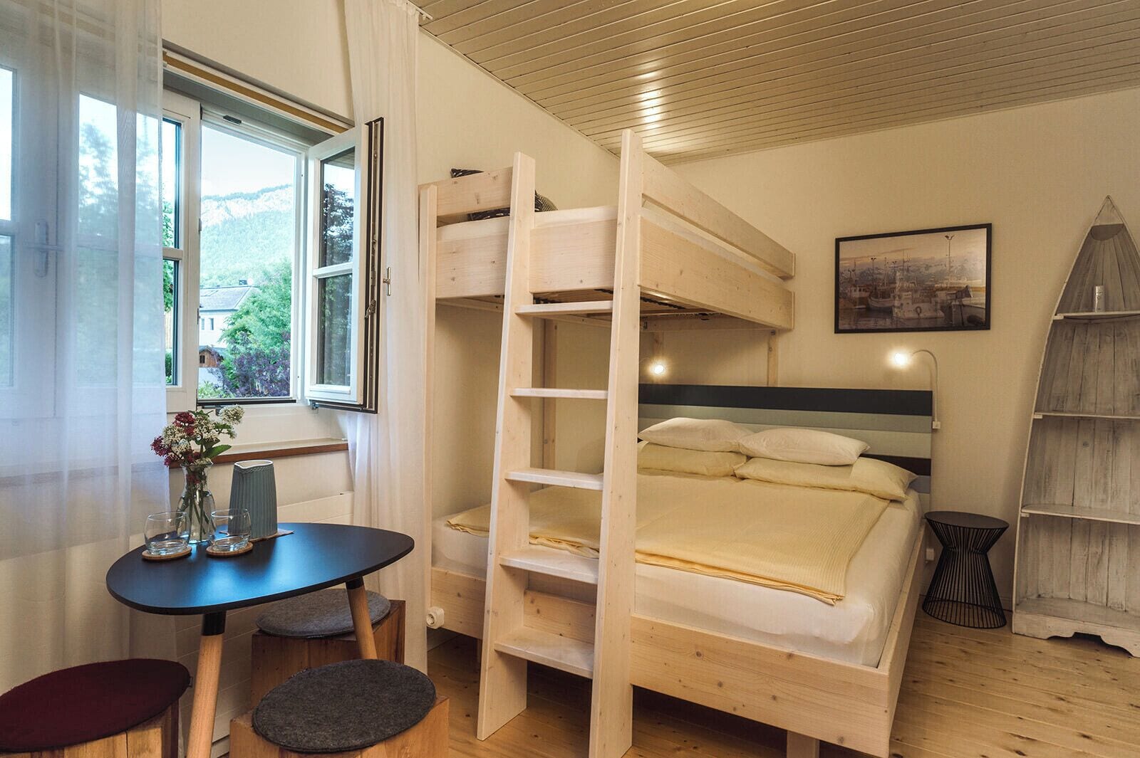 A room with bunk beds, a small table with a vase, a chair, and a window with curtains.