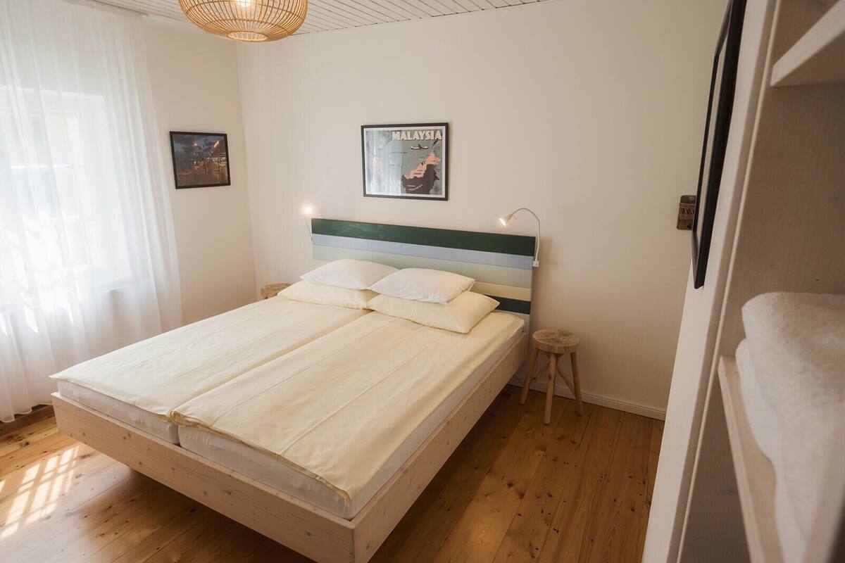 A bedroom with a bed, a headboard, a nightstand, a framed map, and a window with curtains.