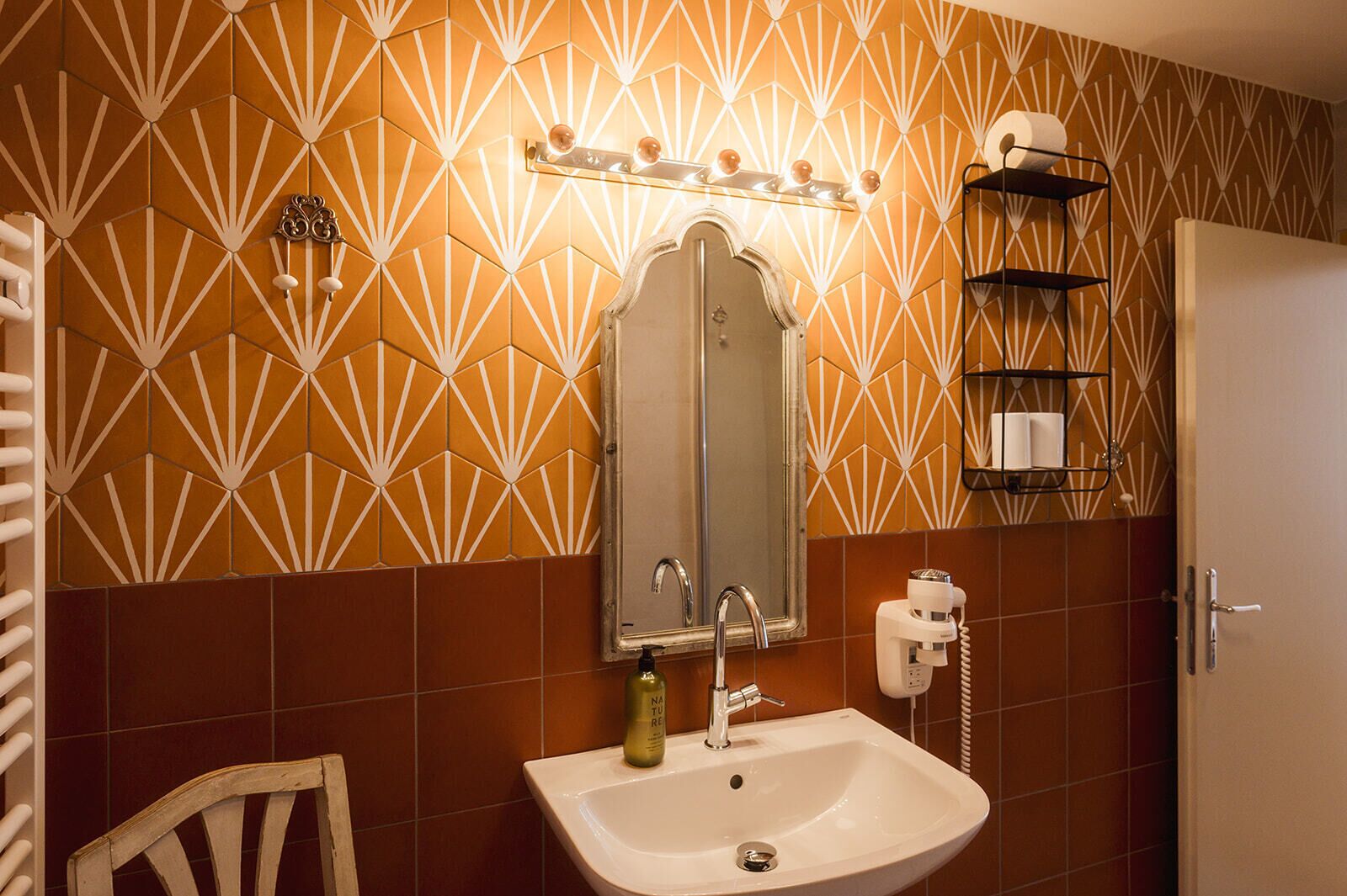 Un baño con lavamanos, espejo, toallero y pared con diseño.