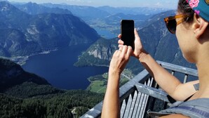 Una persona sosteniendo un teléfono inteligente, contemplando un paisaje montañoso con un lago.