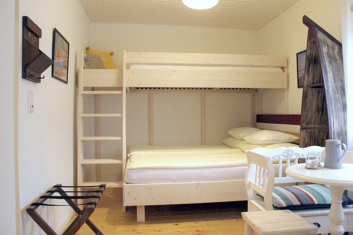 A bunk bed with a ladder, a small table with a pitcher and glass, and a chair with a striped cushion.