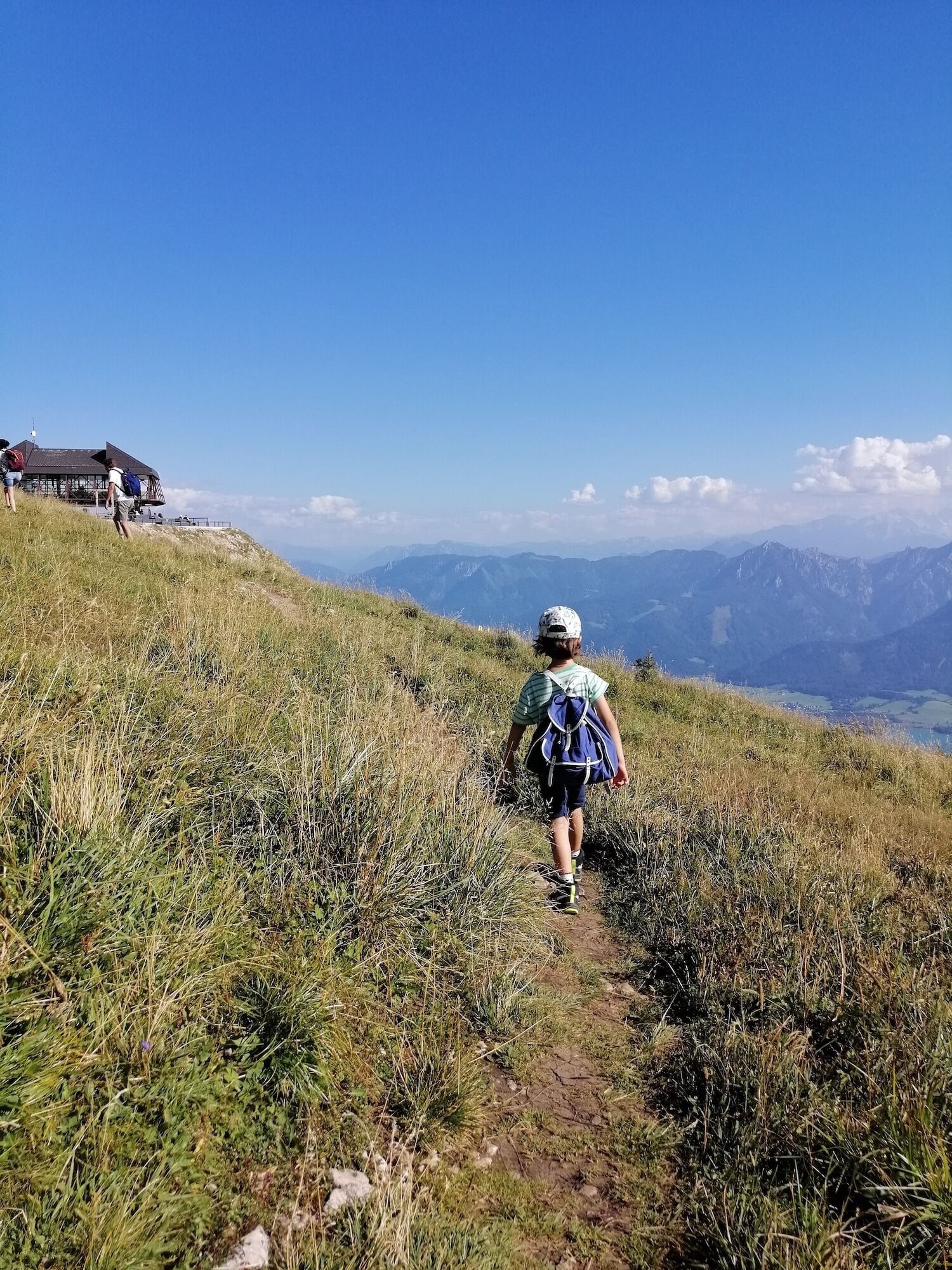 Ein Wanderer auf einem grasbewachsen Pfad mit Blick auf die Berge.
