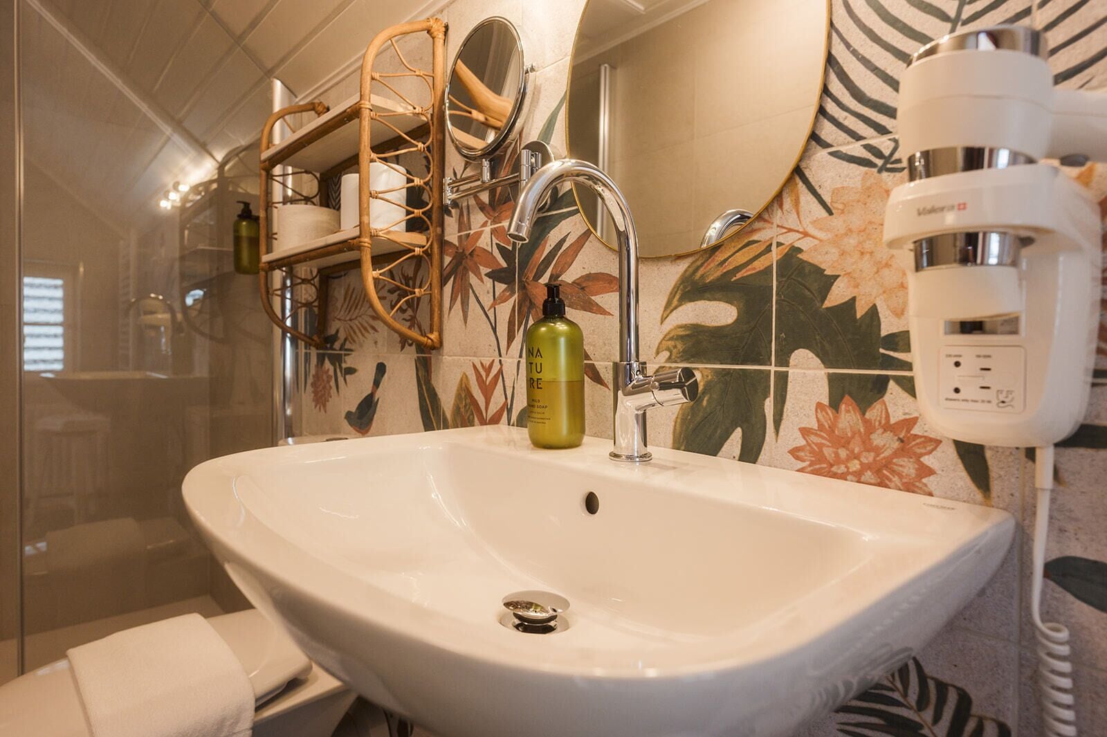 Un baño con un lavamanos blanco, un espejo, una ducha y un perchero para toallas.