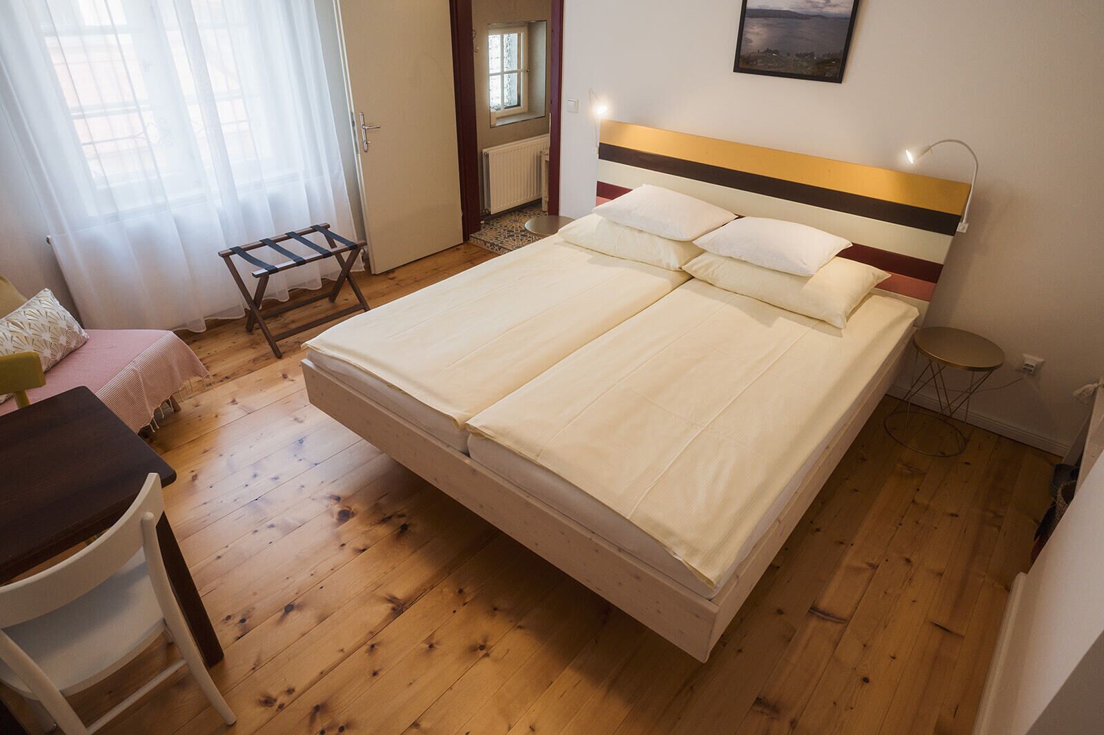 A bedroom with a bed, a chair, a small table, a radiator, and a window with curtains.