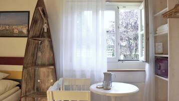 Une pièce avec une échelle en bois, une petite table sur laquelle se trouve une carafe, une chaise, une fenêtre donnant sur des arbres et un lit avec un oreiller.