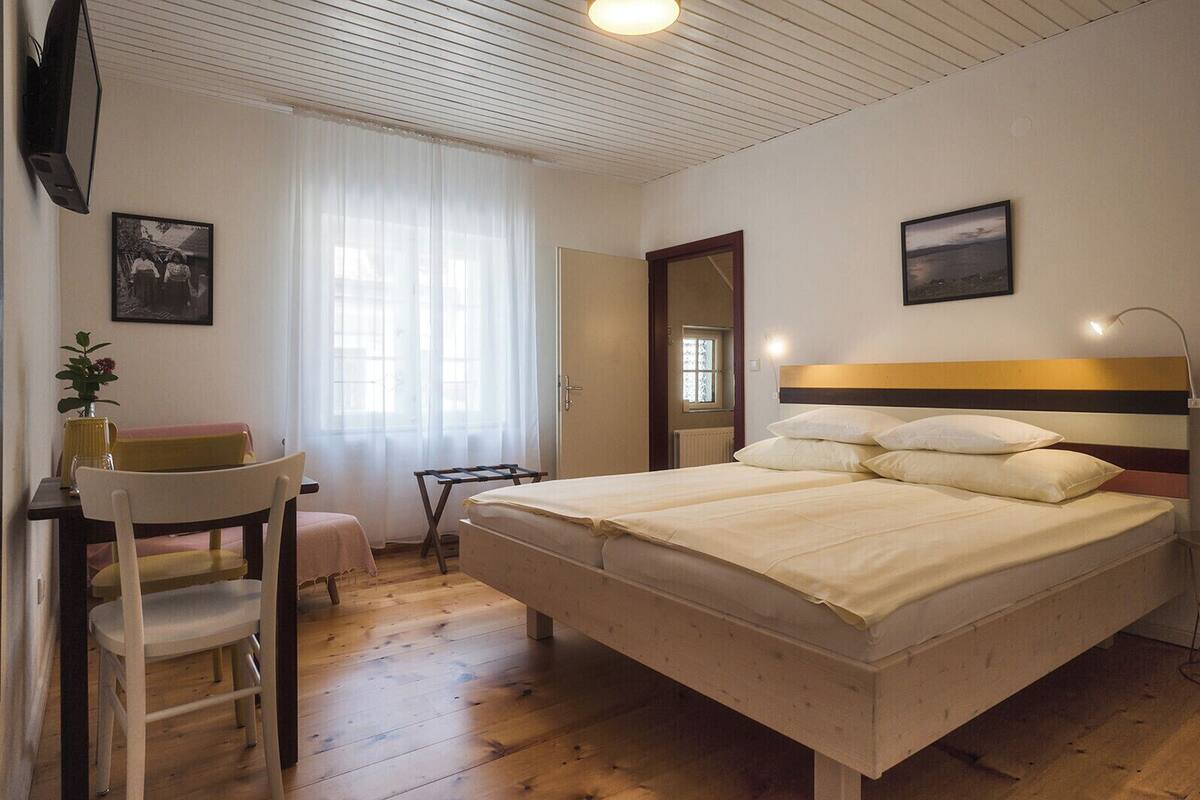 A bedroom with a bed, a desk, a chair, a window with curtains, and a door.