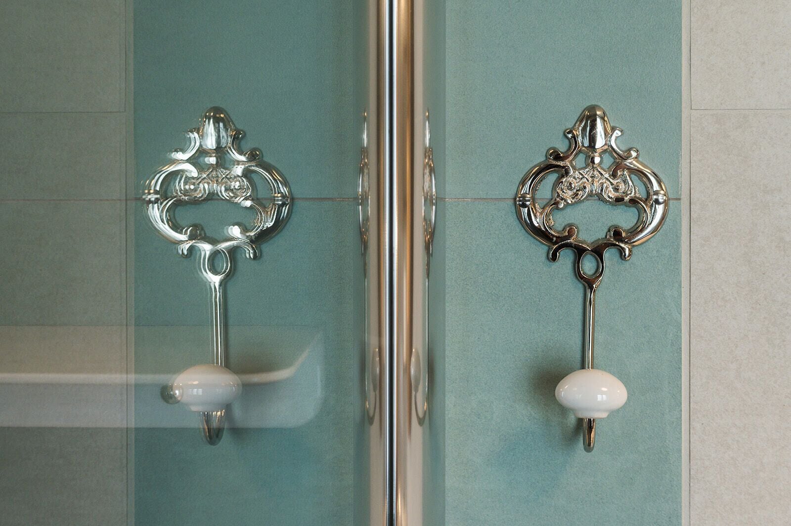 Casa de banho com duas maçanetas de prata ornamentadas e botões de cerâmica branca.