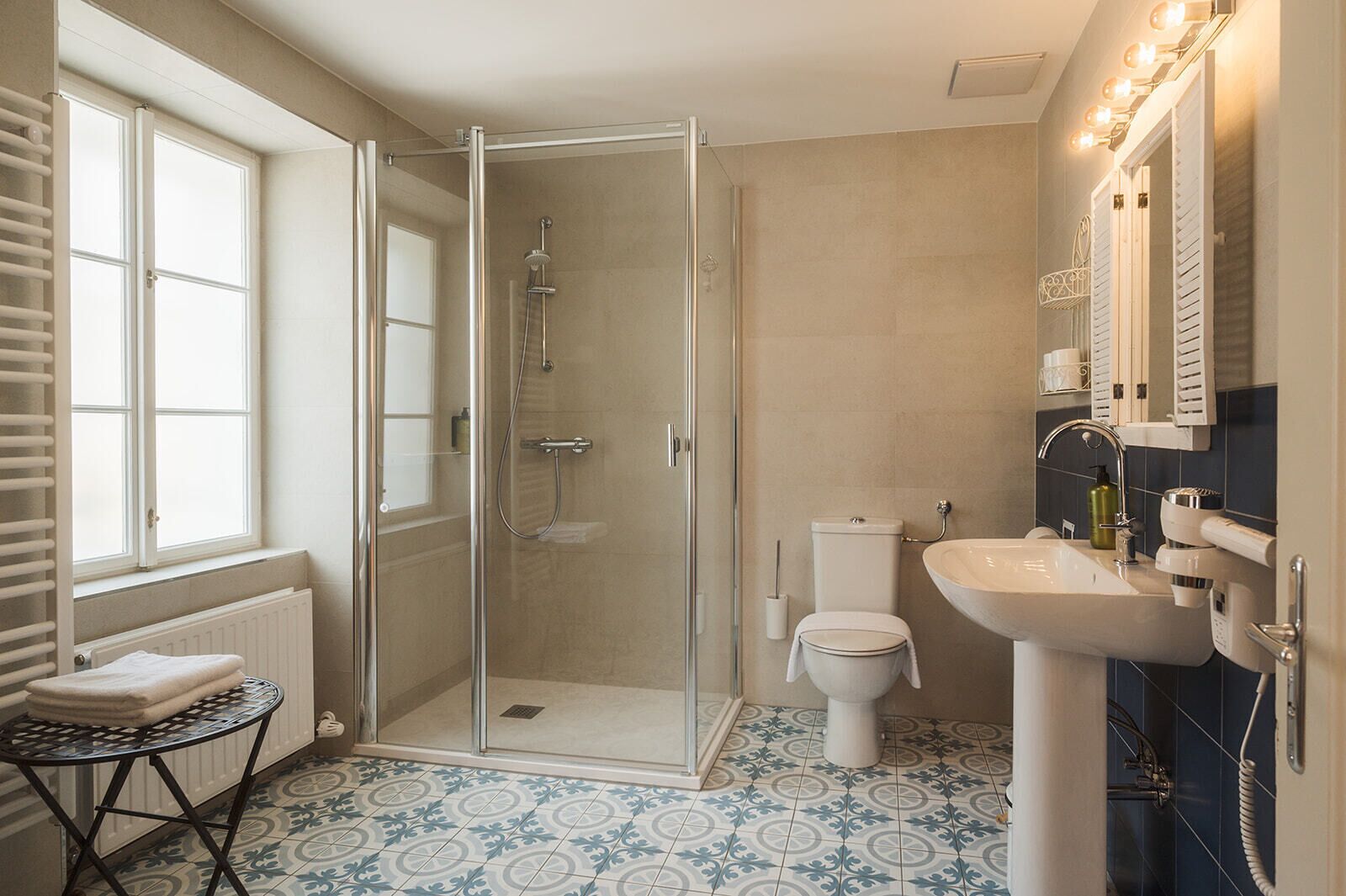 A bathroom with a glass shower enclosure, a toilet, a sink with a mirror, and a radiator.