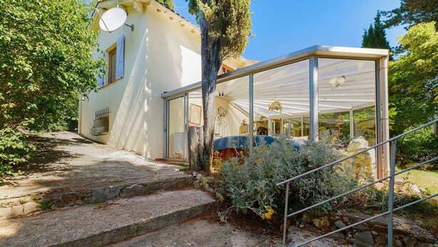 A white building with a covered outdoor area, stone steps leading to a door, and a garden with various plants. - Villa "La Lufrerie": Mountain Views, Private Pool & Wi-Fi (Sospel)