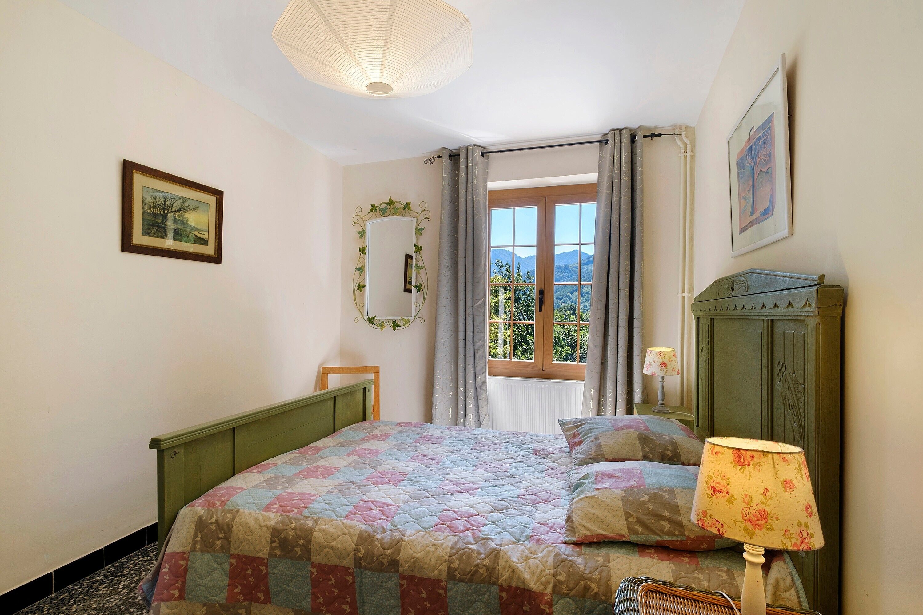 Une chambre à coucher avec un lit, une fenêtre avec des rideaux, un miroir et une lampe.