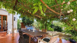 An outdoor patio with a wooden table and chairs, surrounded by lush greenery and a pergola. - Villa "La Lufrerie": Mountain Views, Private Pool & Wi-Fi (Sospel)