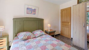 A bedroom with a bed, a nightstand, a lamp, a wardrobe, and a painting on the wall. - Villa "La Lufrerie": Mountain Views, Private Pool & Wi-Fi (Sospel)