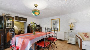 A dining area with a table set for four, a chandelier, and a white sofa with a floral cushion. - Villa "La Lufrerie": Mountain Views, Private Pool & Wi-Fi (Sospel)