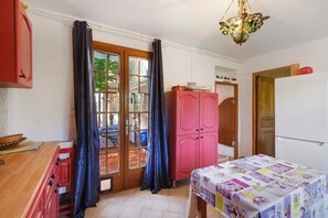A kitchen with a refrigerator, a pink cabinet, a table with a floral tablecloth, and a window with curtains.