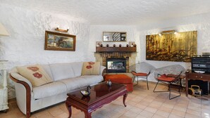 A living room with a sofa, a coffee table, a fireplace, and a painting on the wall. - Villa "La Lufrerie": Mountain Views, Private Pool & Wi-Fi (Sospel)