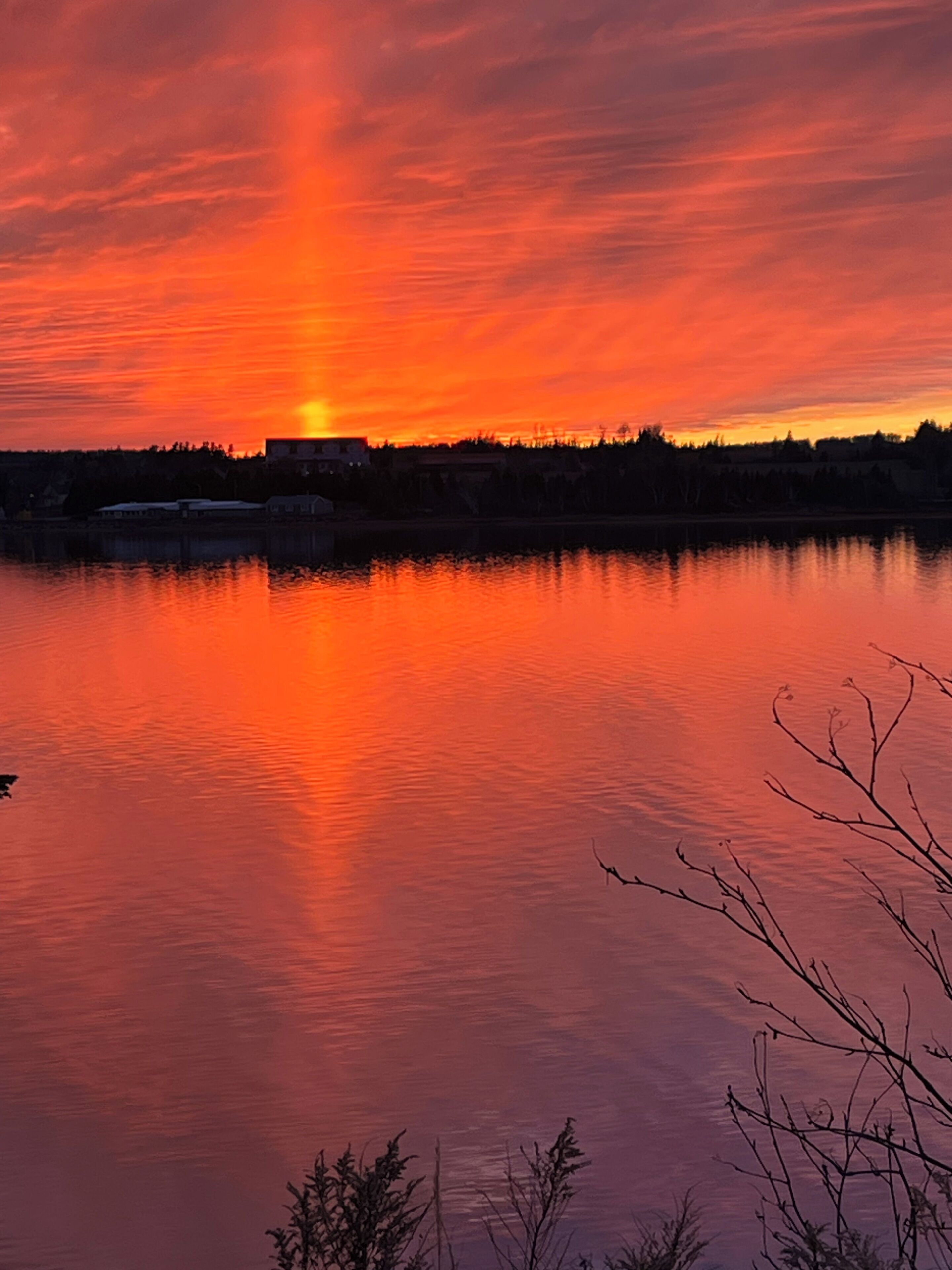 A sunset over a calm lake with a silhouette of trees and buildings in the background.
