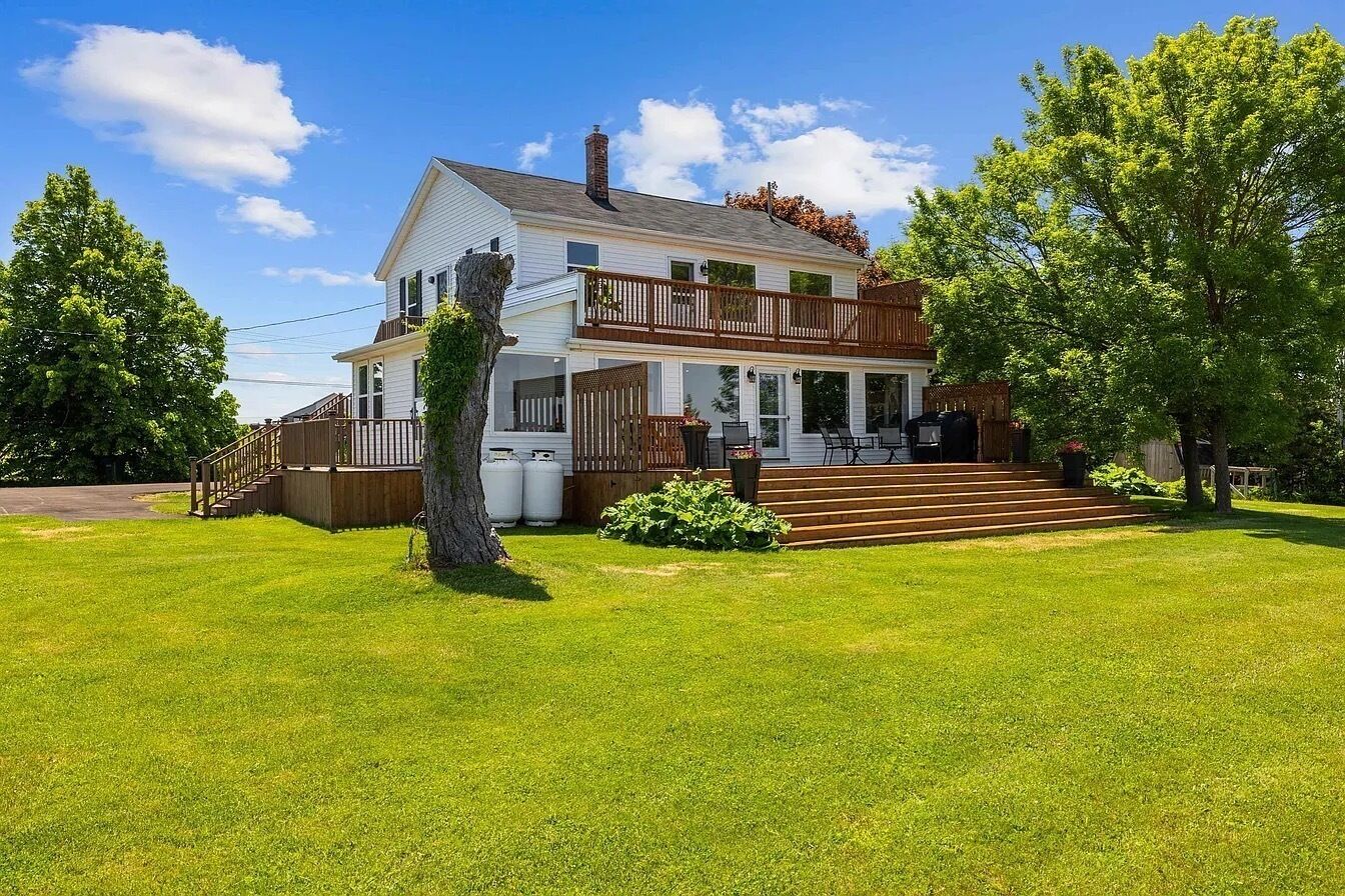 Ein zweigeschossiges Haus mit einer Veranda, einer Holzterrasse und einem gepflegten Rasen.