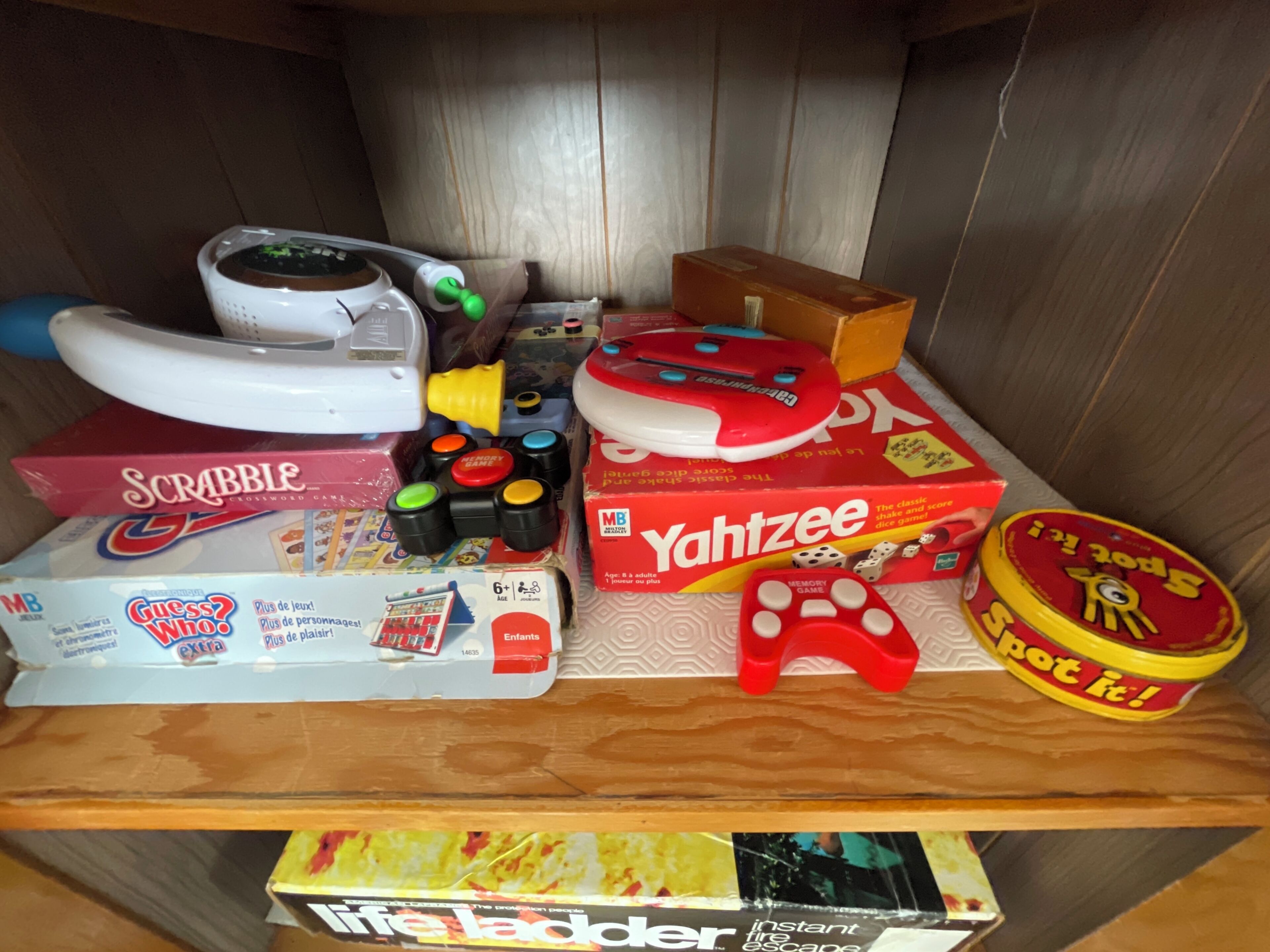 Uma estante com vários jogos de tabuleiro, incluindo Scrabble, Yahtzee e Escalera.