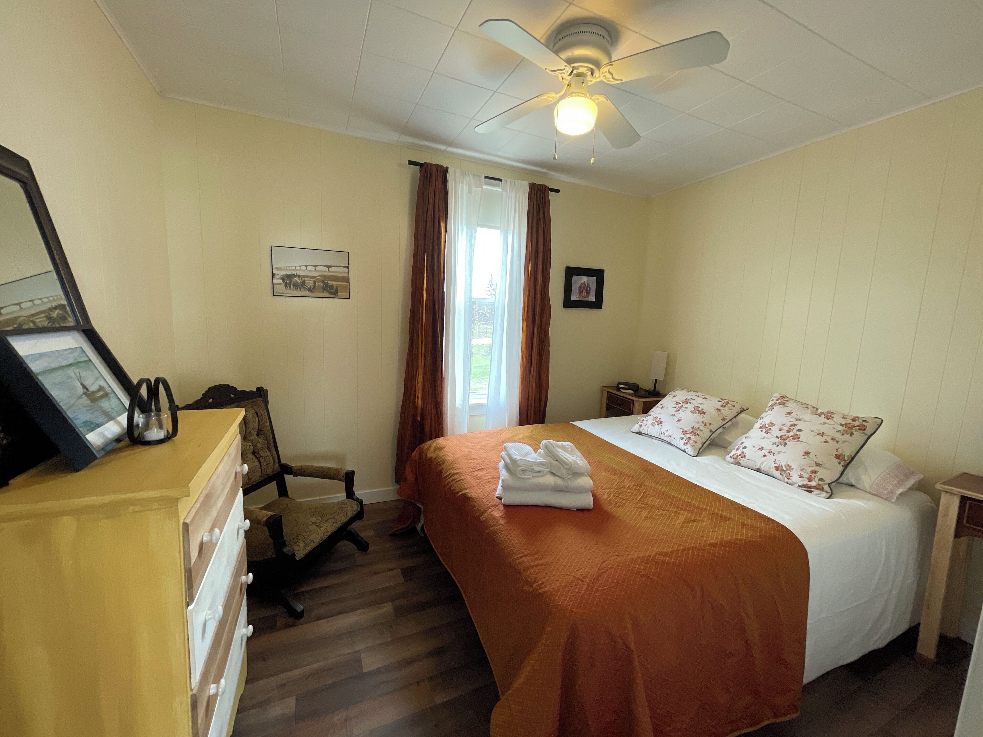A hotel room with a bed, a desk, a chair, a ceiling fan, and a window with curtains.