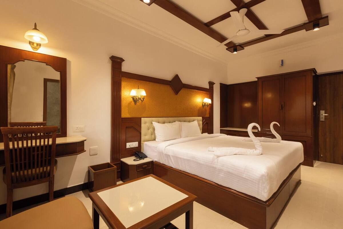 Une chambre d’hôtel avec un grand lit, une tête de lit en bois, une table de chevet, un bureau, un miroir et une armoire.