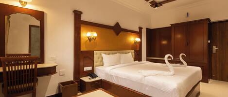 A hotel room with a large bed, a wooden headboard, a nightstand, a desk, a mirror, and a wardrobe.