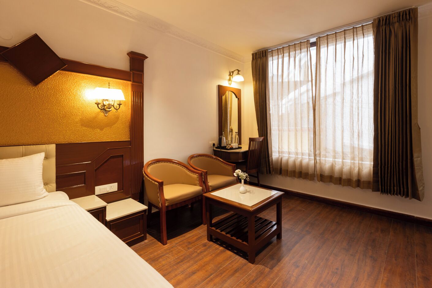 A hotel room with a bed, two armchairs, a small table, a mirror, and a window with curtains.