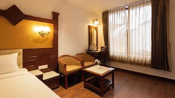A hotel room with a bed, two armchairs, a small table, a mirror, and a window with curtains.