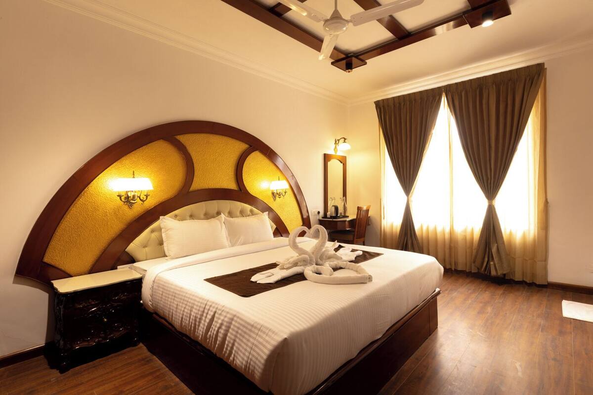 Une chambre d’hôtel avec un grand lit, une table de chevet, un miroir et une fenêtre avec des rideaux.