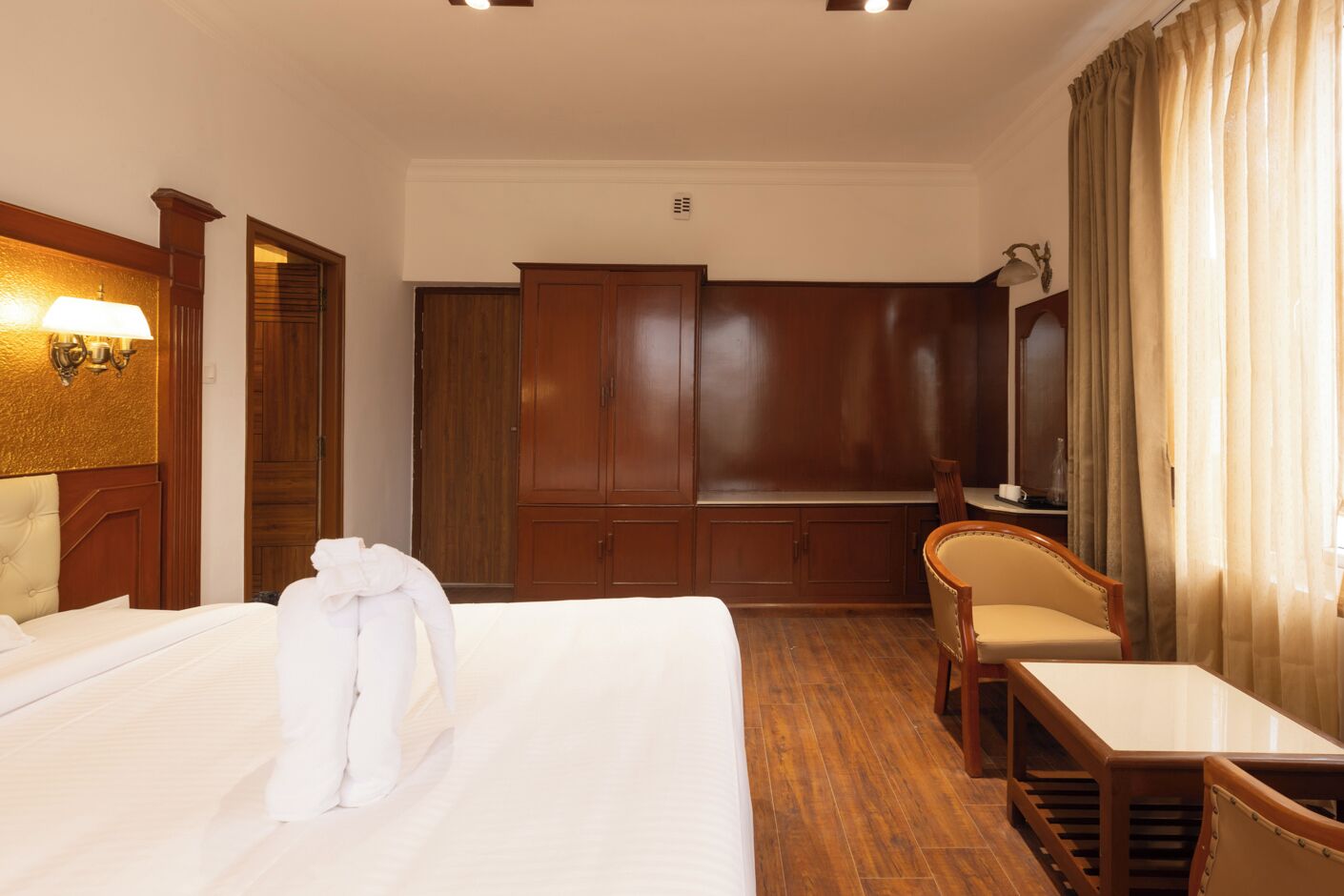 A hotel room with a large bed, a desk, a chair, a wardrobe, and a television.