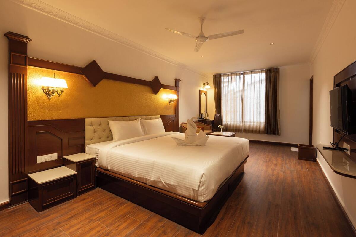 Une chambre d’hôtel avec un grand lit, une télévision, un ventilateur de plafond et un bureau avec une chaise.