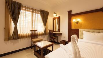 A hotel room with a bed, a desk, a chair, a small table, a mirror, and a window with curtains.