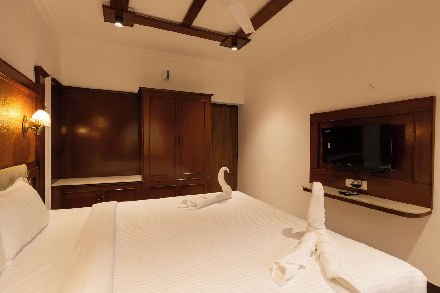 Ein Hotelzimmer mit einem großen Bett, einem Holzschrank, einem Flachbildfernseher und einem Deckenventilator.