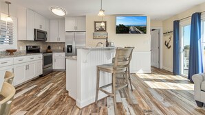Una cocina moderna con armarios blancos, una isla central y un comedor con una silla.