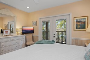 Une chambre à coucher avec un lit, une commode, une télévision et une porte-fenêtre donnant sur un balcon.