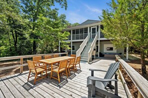 A wooden deck with a dining table and chairs, a covered seating area, and a staircase leading to a building. - Hark the Sound | Soundfront 4BR w/ Private Pier, Golf Cart & Sunset Views (Emerald Isle)