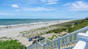 Blick auf einen Strand vom Balkon aus, mit Geländer, Sandstrand, Meer und einigen Personen.