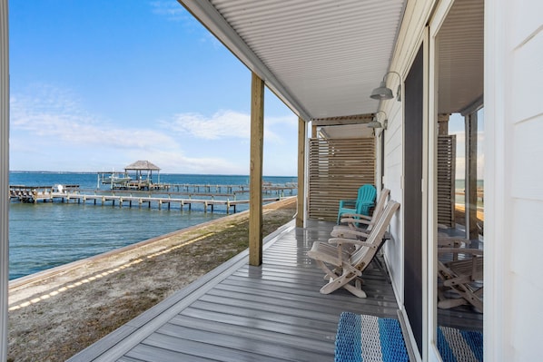 Une terrasse couverte avec des chaises en bois, une vue sur la mer et une jetée en arrière-plan.