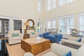 A spacious living room with a beige sofa, a blue sofa, and a wooden coffee table. There is a mirror on the wall and a door with an exit sign. - Ocean Club J-202 | Oceanside 3BR Condo w/ Pools, Hot Tubs & Resort Amenities (Indian Beach)