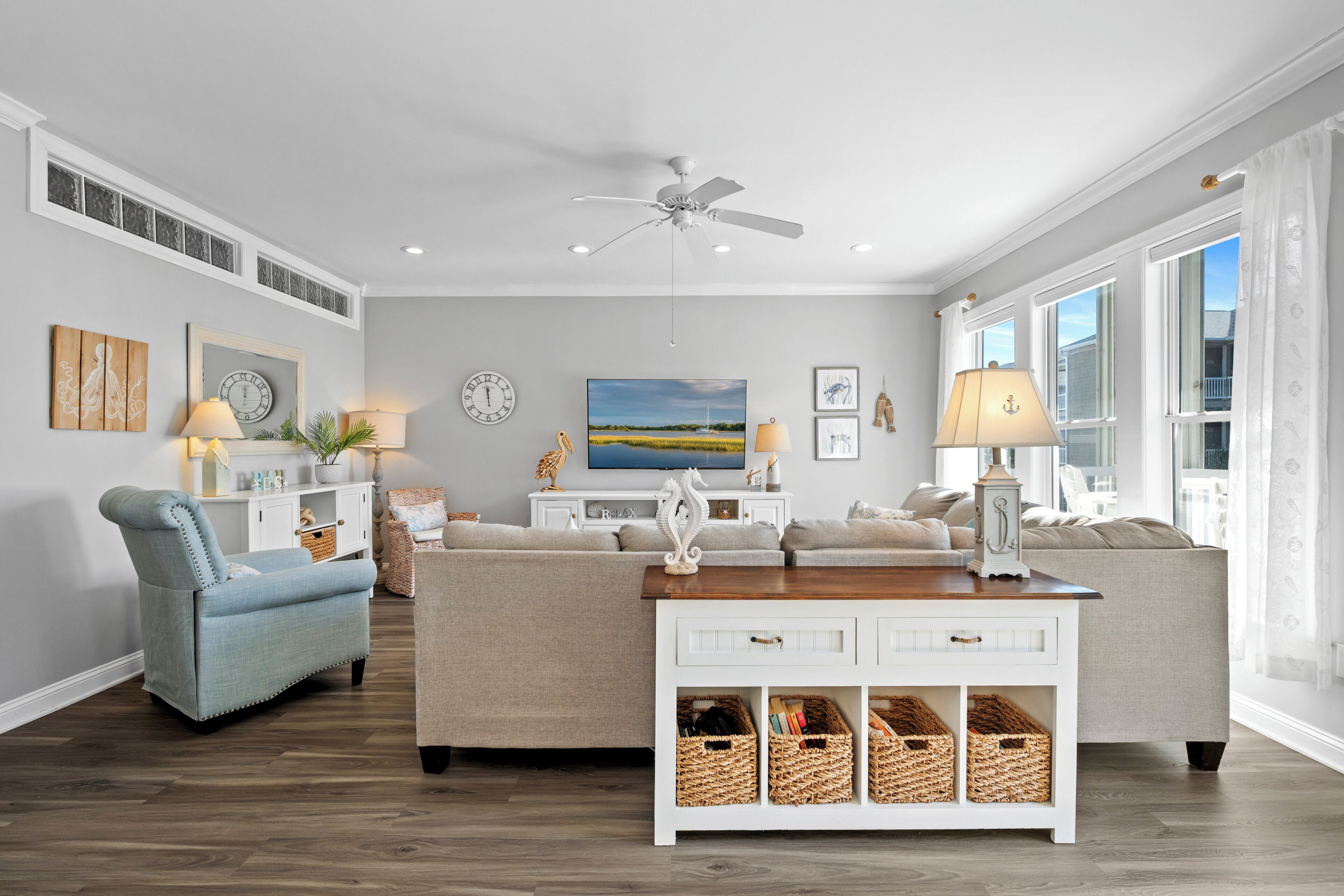 A living room with a ceiling fan, a large window, a sofa, a coffee table, and wall art.