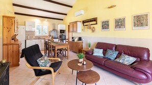 Un salon avec un canapé, des fauteuils, une table à manger et, au fond, une cuisine.