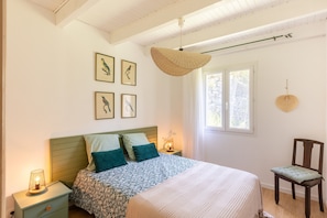 A bedroom with a bed, bedside tables, a chair, a window, and wall art.