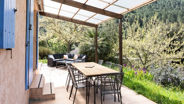 Une terrasse couverte avec une table et des chaises en bois, un canapé et un barbecue.