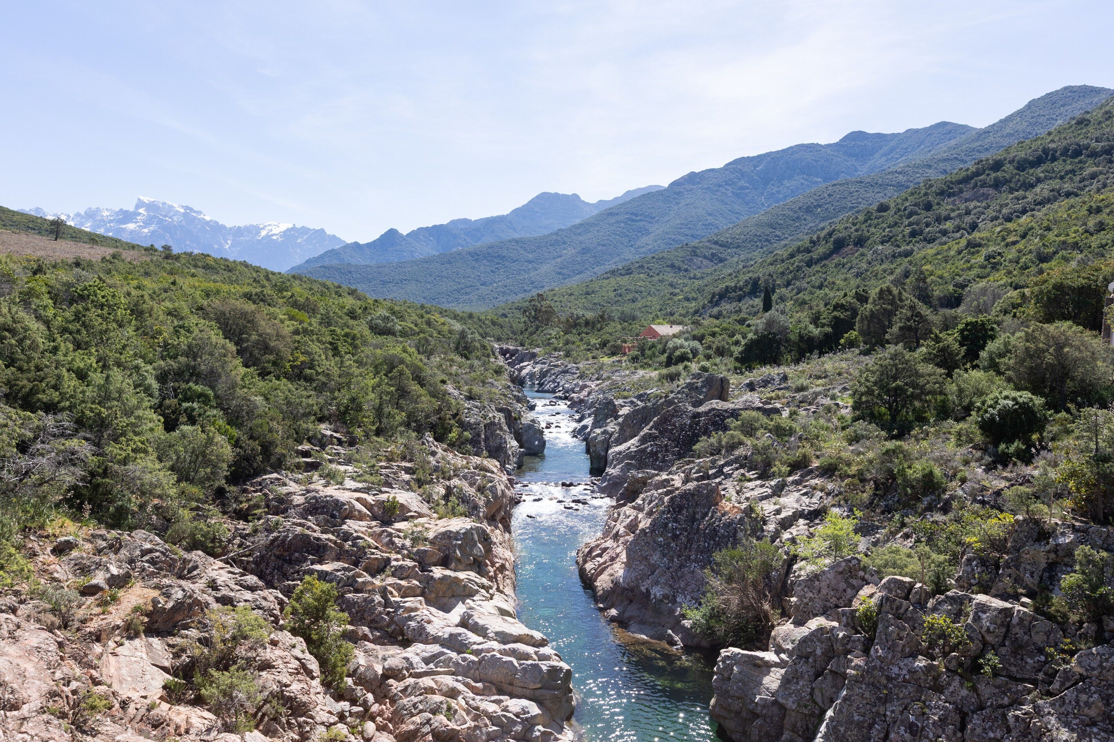 A mountainous landscape with a river, rocky terrain, and a small building.